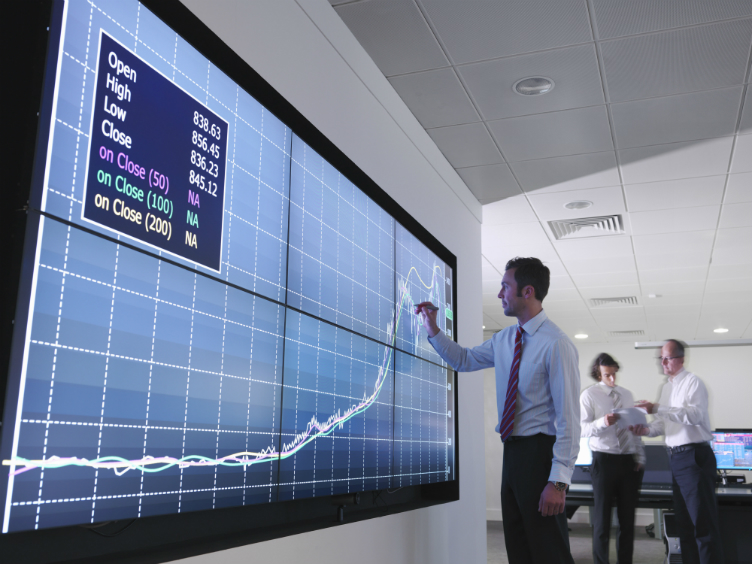 Man in front of board showing share performance